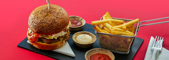 Hamburger, fries and dipping sauces on a red background